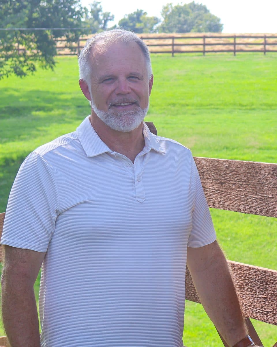 Rohmel at a wooden pasture gate with green fields behind him
